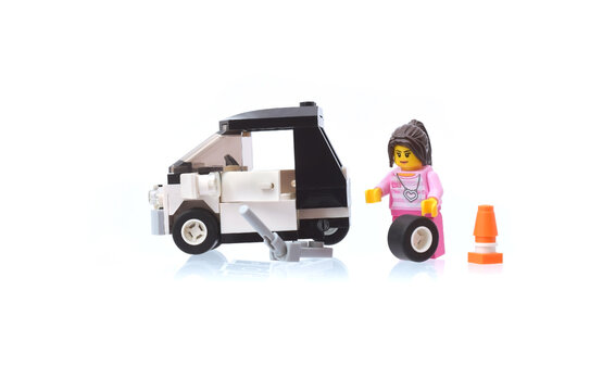 Lego minifigure of autolady is changing a wheel of car. Editorial illustrative image of popular plastic bricks toy. Studio shot.