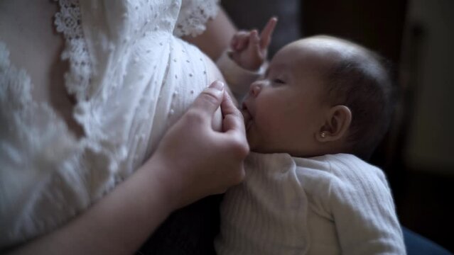 beb&eacute; succionando de pecho de madre sentada en sof&aacute; de casa mientras hijo intentando dormir