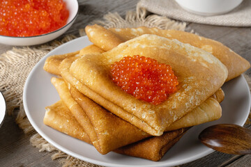 Stack of russian thin pancakes blini with red caviar on an old wooden table. Maslenitsa, traditional Russian blini