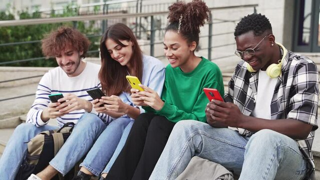 University Students sitting in stairway typing on smartphones - Multicultural group of friends using cell phones 