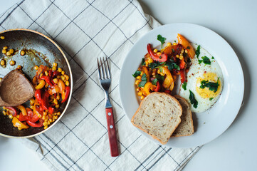 tasty vegetarian farm style breakfast - fried egg with baked sweet peppers and corn with parsley and whole grain bread served on white plate
