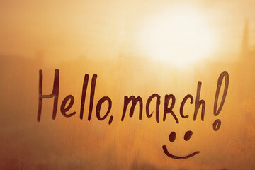 Handwritten text Hello march and smile on wet orange window