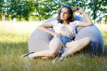 Young woman sitting outside on a sofa in nature on a sunny summer day