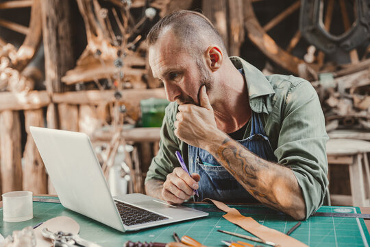 Leather artist hipster looking at computer laptop screen serious thinking for learning or contact customer