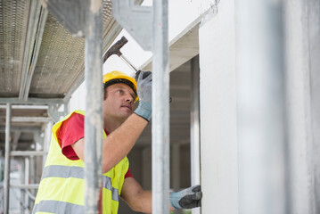Construction worker with hammer at building site verifying the material