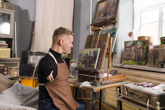 a young man with disabilities paints a picture with oil paints in an art workshop.