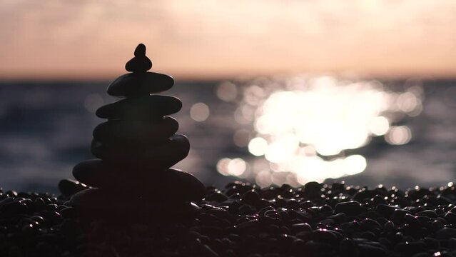 Pyramid stones on the seashore with warm sunset on the sea background. Happy holidays. Pebble beach, calm sea, travel destination. Concept of happy vacation on the sea, meditation, spa, calmness.