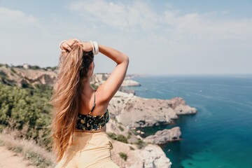 Fototapeta na wymiar Woman travel sea. Happy tourist enjoy taking picture outdoors for memories. Woman traveler looks at the edge of the cliff on the sea bay of mountains, sharing travel adventure journey