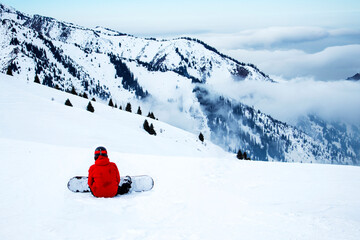 a snowboarder in a red jacket is sitting on a mountainside