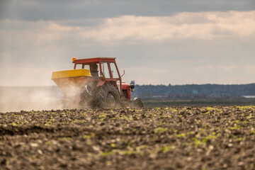 Fototapeta premium Farmer in an agricultural tractor at a farm fertilizing an arable field, ensuring a successful harvest