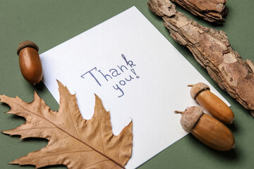 Paper sheet with text THANK YOU, acorns, leaf and tree bark on green background