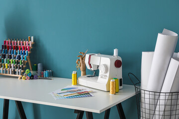 Tailor's workplace with sewing machine and threads near blue wall