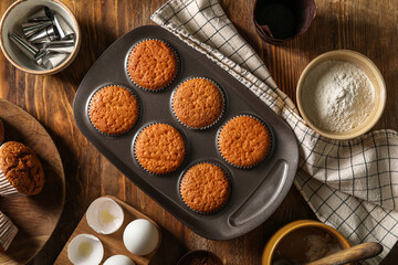 Tray with tasty muffins, ingredients and piping tips on wooden background