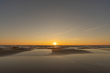 Fototapeta premium Sunset in a cloudless sky on the coast of the Gulf of Finland in Ust-Narva. The sky is clear, the waves gently roll on the sand. Estonia, Narva-Jyesuu. Natural background. Space for text.