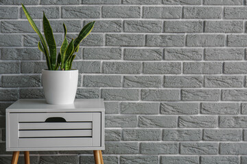 White table with drawer and houseplant near grey brick wall