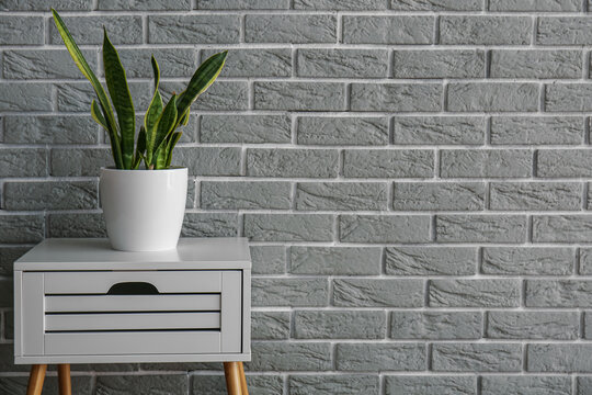 Fototapeta White table with drawer and houseplant near grey brick wall