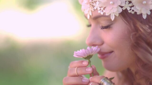 Cropped closeup of a girl in boho style vintage lace headband smiling while smelling a fresh pink daisy flower in nature