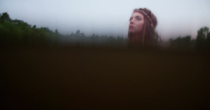 Closeup of a beautiful hippie girl submerged in dark water wearing a headband and looking away dreamily