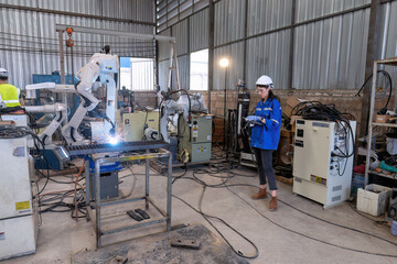 In robotic maintenance shop girl engineer hold controller operate robot arm welding fire spark