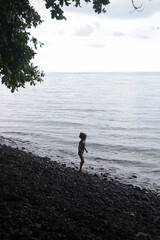 Adorable little girl on the huge empty black pebbled beach