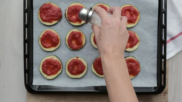 Manos de mujer ponen sal sobre tomate natural triturado y rodajas de berenjena en una bandeja de horno