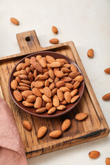 Wooden board with plate of almond nuts on light background