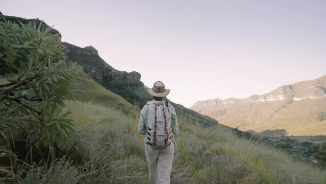 Handheld rear view shot of female hiker with backpack walking on mountain against clear sky