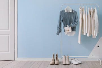 Rack with stylish clothes, bag and shoes near color wall