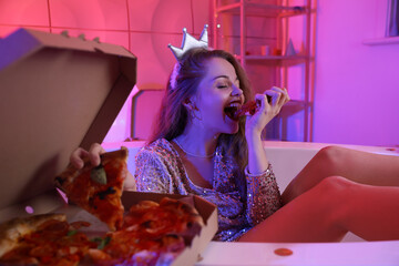 Young woman eating tasty pizza in bathtub after party