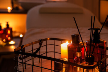 Fototapeta na wymiar Basket with cosmetic products, burning candles and reed diffuser in dark spa salon, closeup