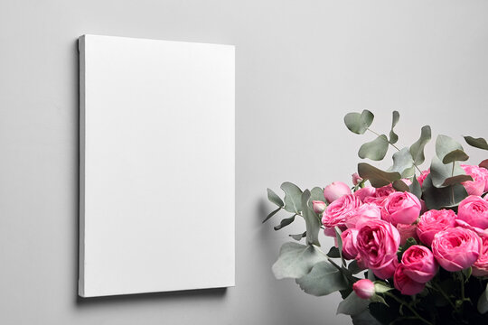 White canvas mockup hanging on grey wall and bouquet of pink roses with eucalyptus leaves. Blank canvas, interior decor