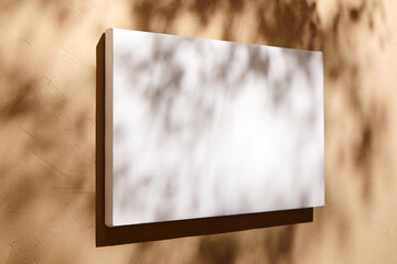 White canvas, blank picture mockup hanging on beige wall with dark shadows of leaves. Poster...