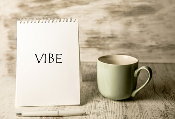 Vibe inscription on a notebook and a cup on the table.