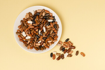 Brown bean mix in white plate and scattered on a beige or yellow background top view