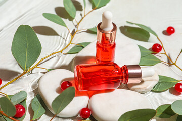 Composition with bottles of serum, spa stones, cranberry and eucalyptus branches in water on light background, closeup