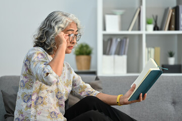 Elderly woman trying to read book having difficulties seeing text because of vision problems