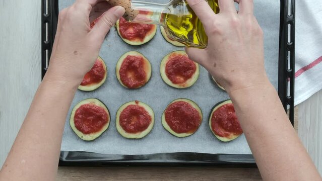 Manos de mujer ponen aceite sobre rodajas de berenjena con orégano y tomate natural triturado en una bandeja de horno