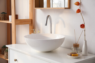 Ceramic sink, vase with plant branch and bath accessories on drawers in bathroom