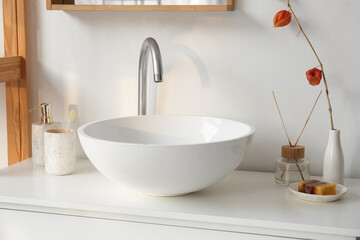 Ceramic sink, vase with plant branch and bath accessories on drawers in bathroom