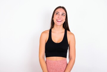 young woman wearing sportswear over white studio background with broad smile, shows white teeth, feeling confident rejoices having day off.