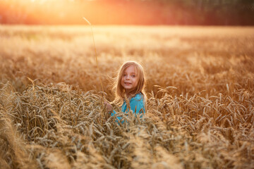 smiling little girl in a field with grain during sunset, holiday in the countryside