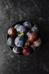 Top view of bowl of fresh picked plums on black background.