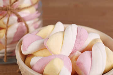 Bowl and jar of delicious twisted marshmallows on brown wooden table