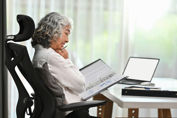 Side view of successful mature businesswoman analyzing financial data while sitting in bright...