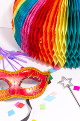 Carnaval or costume party still life with venetian red mask, blowout, magic wand, paper decoration and confetti on white background