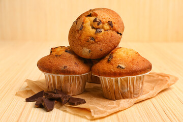 Delicious muffins with chocolate on beige wooden background