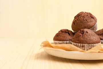 Plate with delicious chocolate muffins on beige wooden background