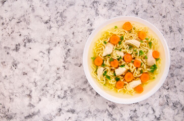 Chicken noodle soup with parsley and vegetables in a white plate,on a gray background.