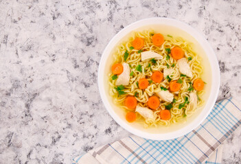 Chicken noodle soup with parsley and vegetables in a white plate,on a gray background.