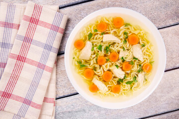 Chicken noodle soup with parsley and vegetables in a white plate,on a gray wooden background.